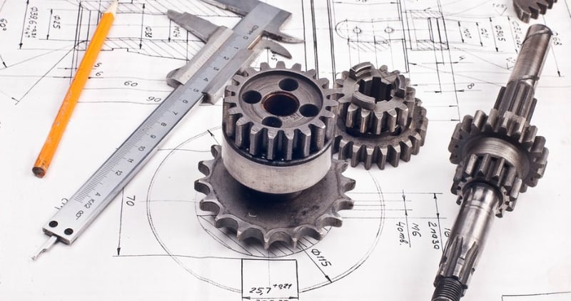 A photo of some cogs, pencils and rulers over a blueprint